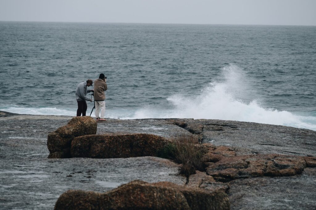 photographers standing on rocky coast and shooting waving sea