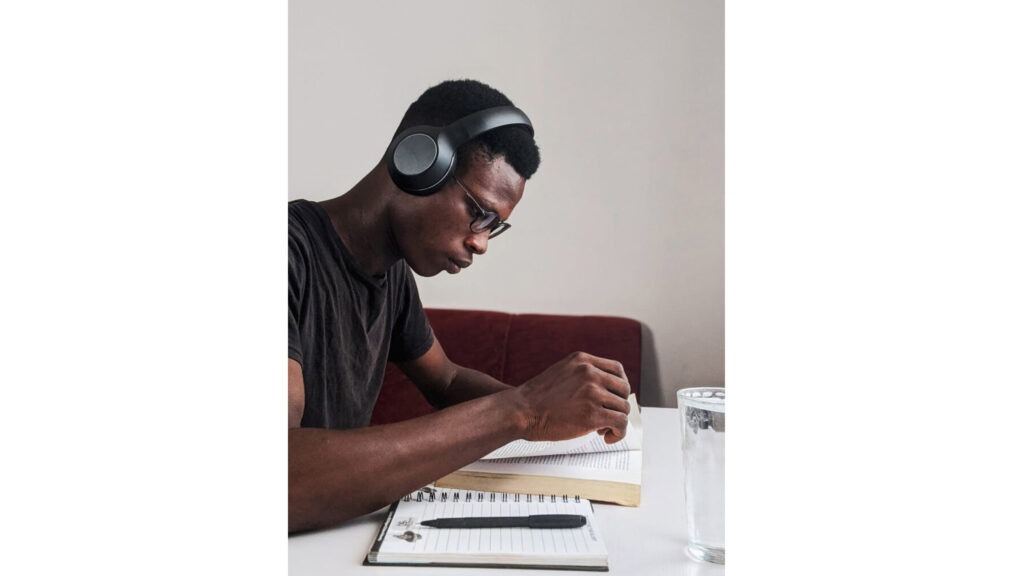 Exam study tips. Man wearing black crew neck t shirt using black headphones reading book while sitting.